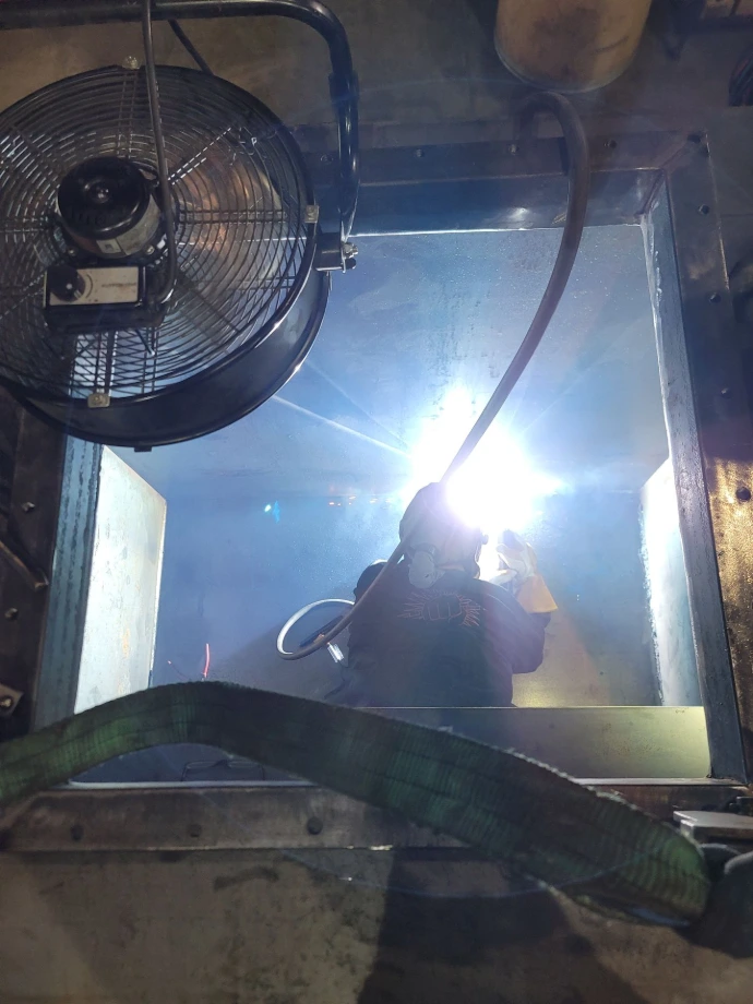 Welder working on a metal assembly beside industrial equipment