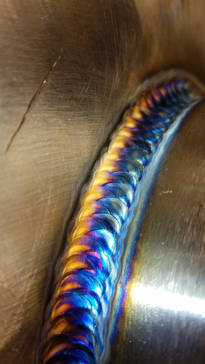 Close-up of a TIG weld with gold, purple, and blue heat coloration
